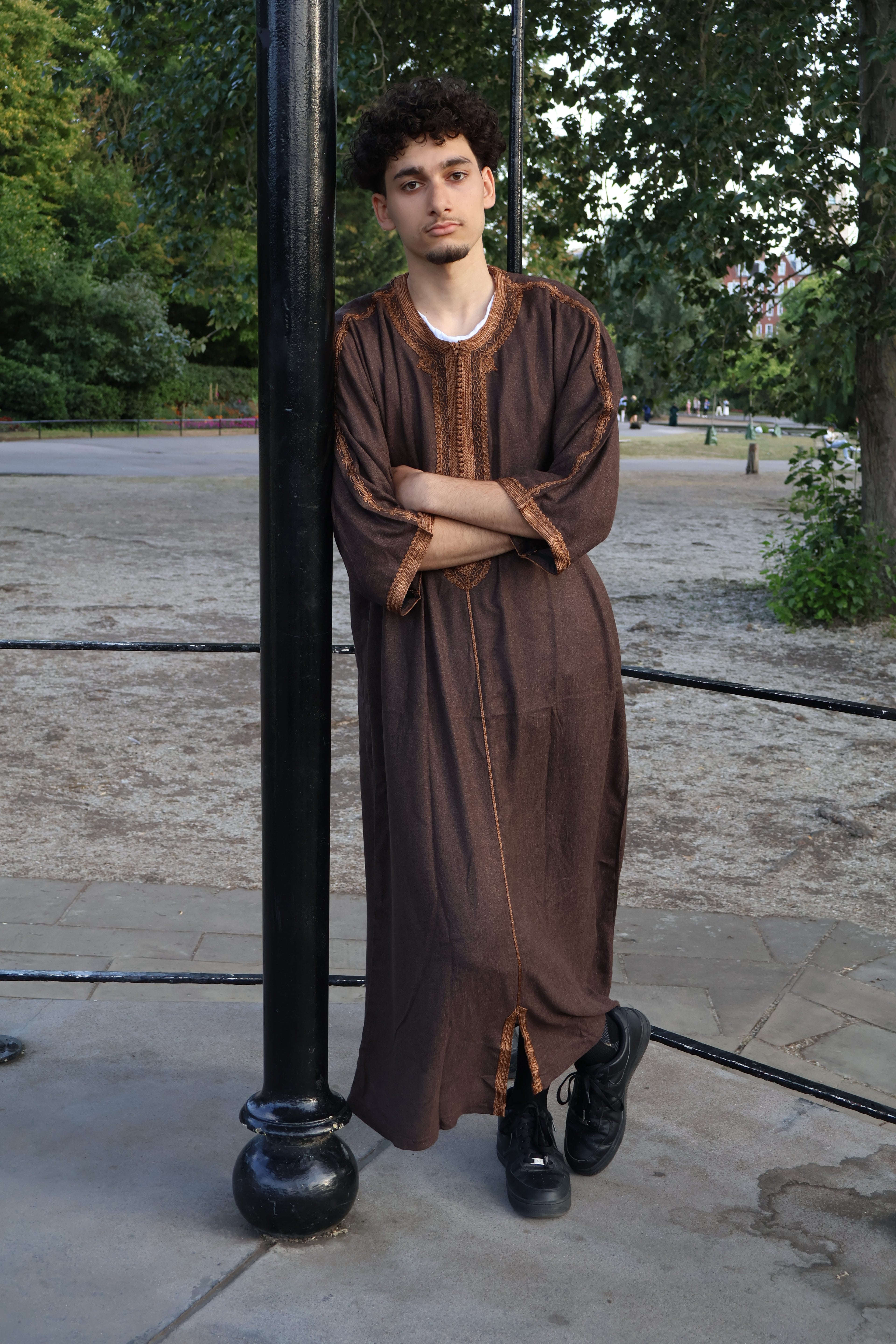 Man with arms crossed, leaning on a pole, wearing a luxurious brown men&