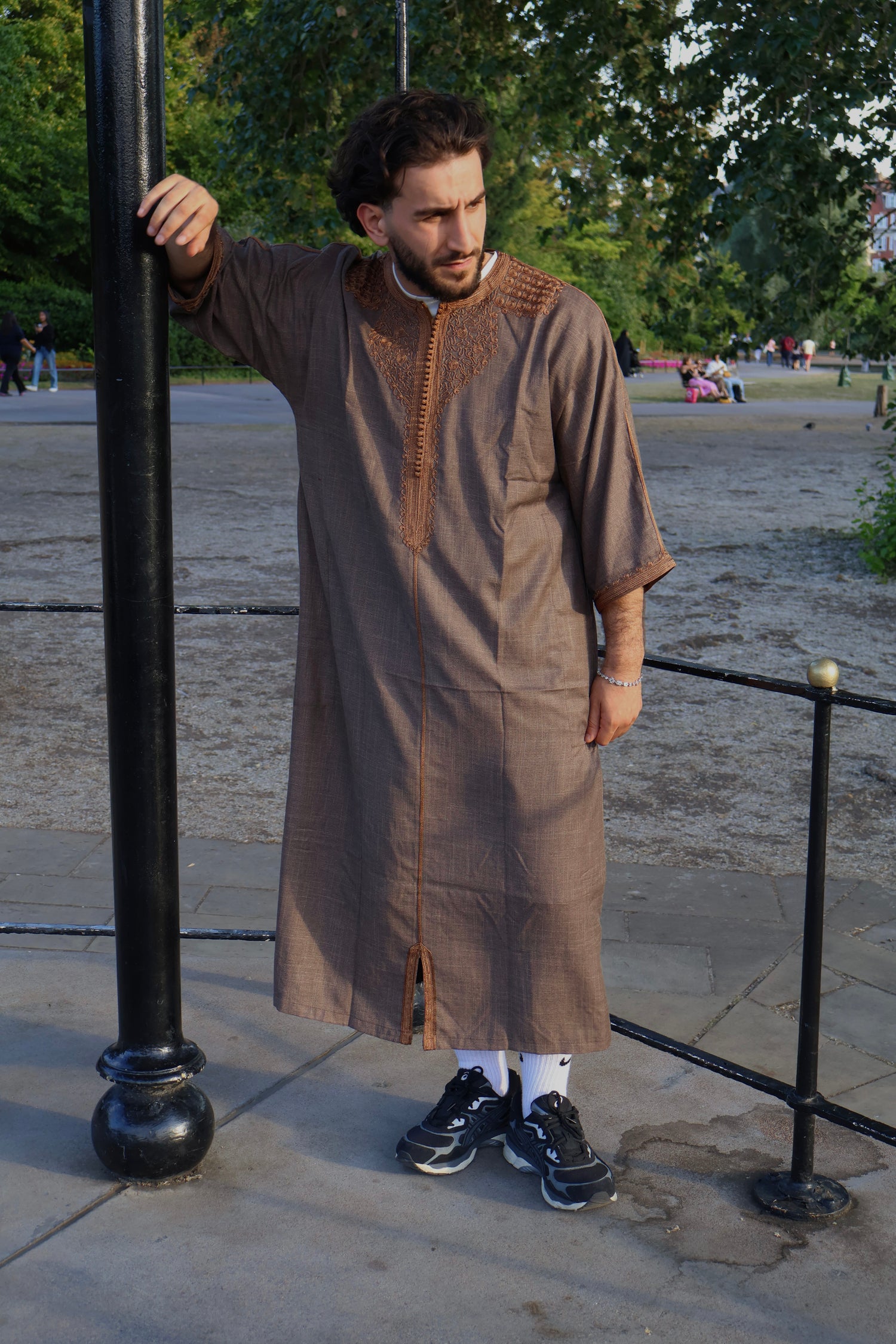 Man outdoors leaning on a black pole, wearing a 